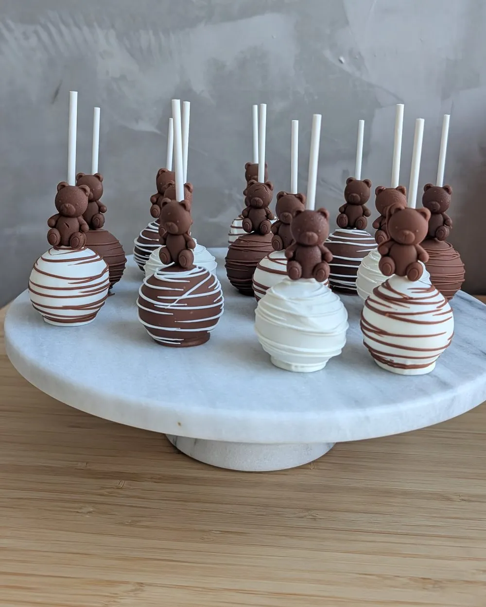 Chocolate cake pops topped with teddy bears on a marble stand