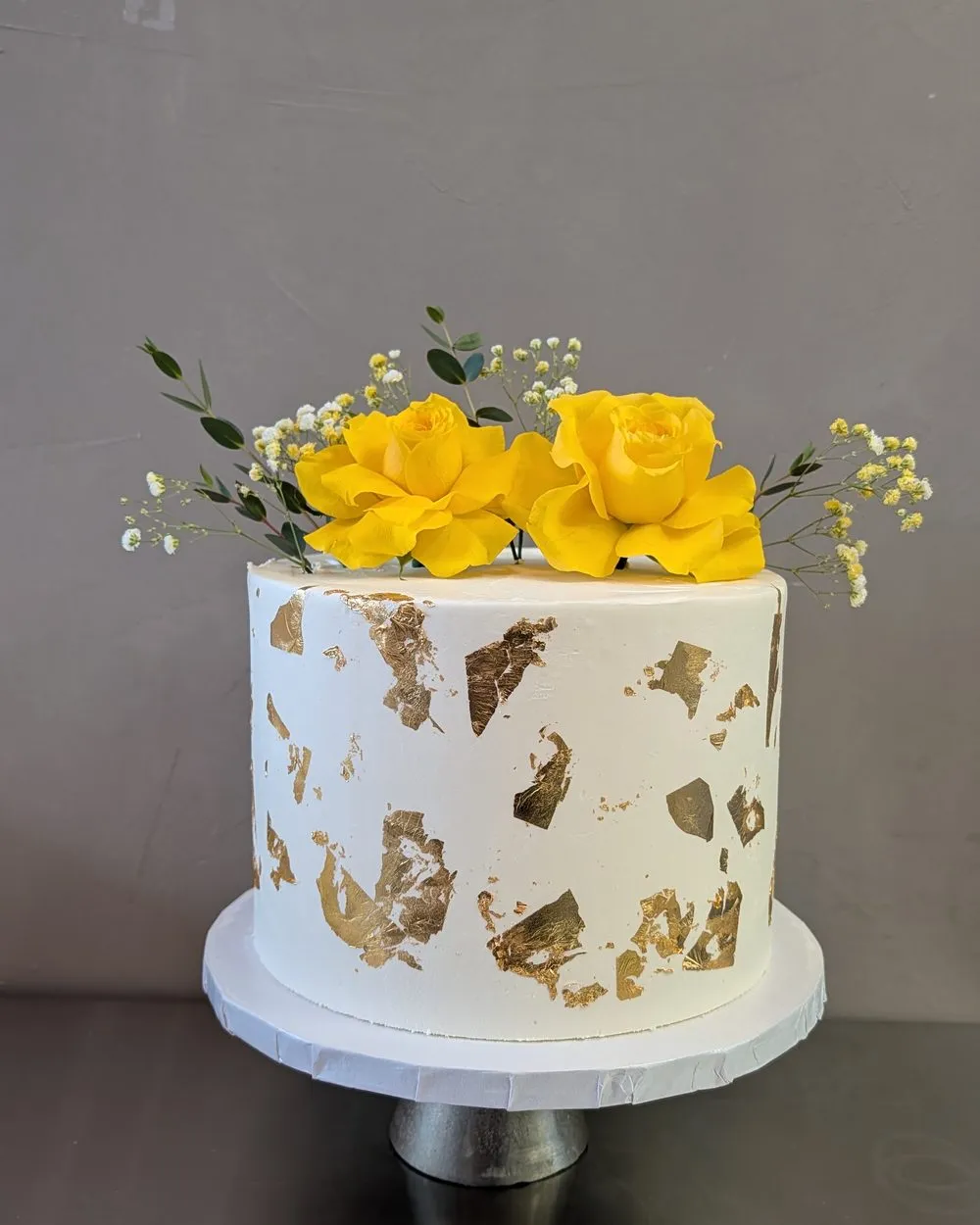 White cake with gold leaf and yellow roses on top