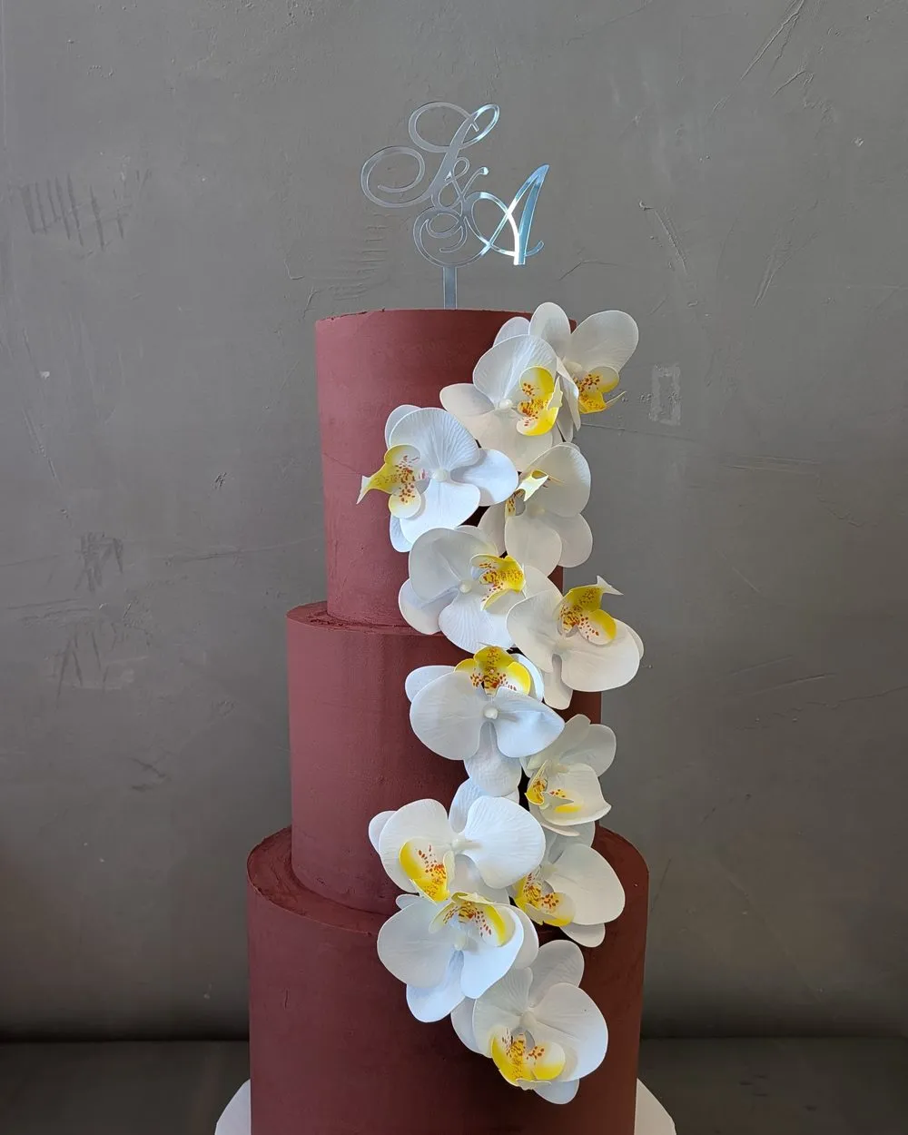 Three-tier wine-red wedding cake with a cascade of white orchids