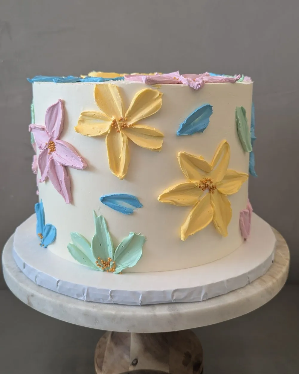 White buttercream cake with painted buttercream flowers in yellow, pink and teal