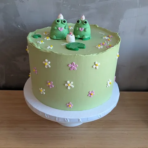 Sage green birthday cake with two fondant frogs and piped daisies