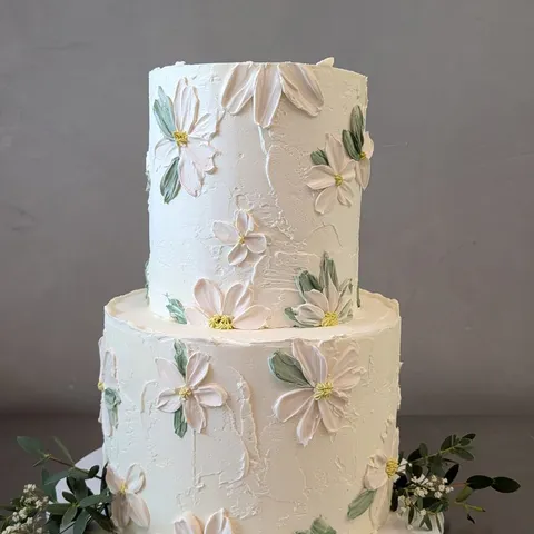Two-tier ivory cake with painted white flowers and greenery