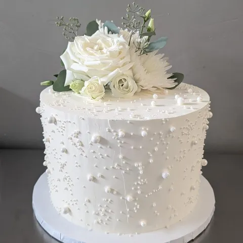 White cake with pearl dots and a spray of white roses